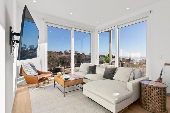 prefab home living room white walls with l-shaped couch, beige rug and floor-to-ceiling windows built by dvele